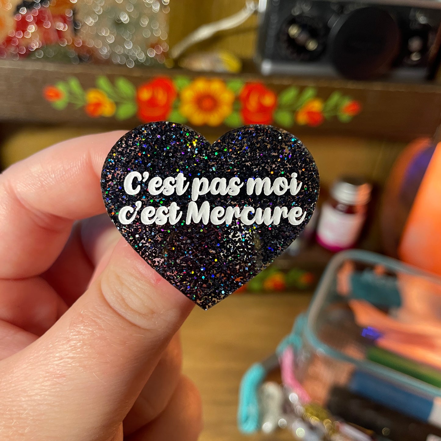 Broche "C'est pas moi c'est Mercure" en acrylique à paillettes noires holographiques