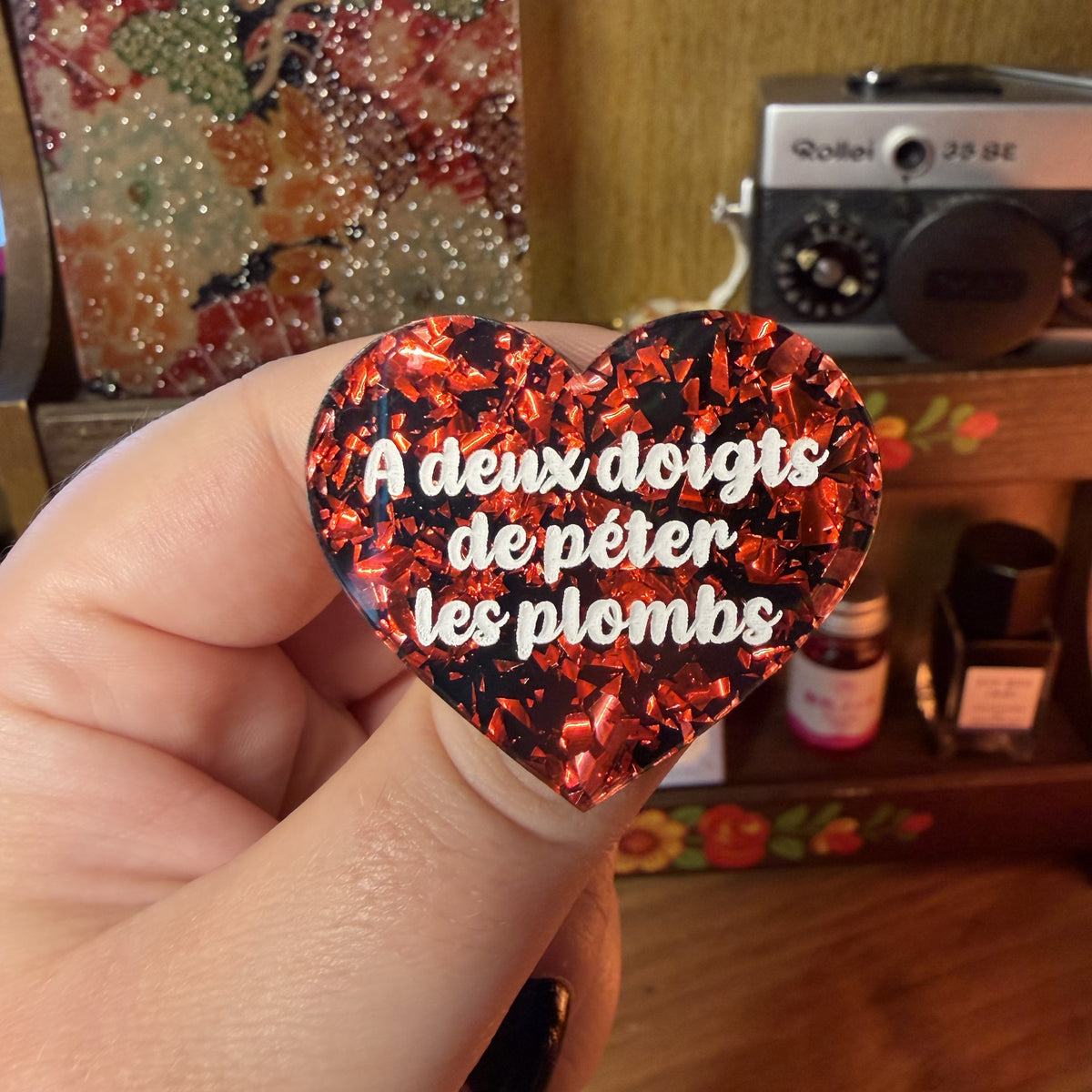 Broche "A deux doigts de péter les plombs" en acrylique noire avec des éclats de confettis rouges