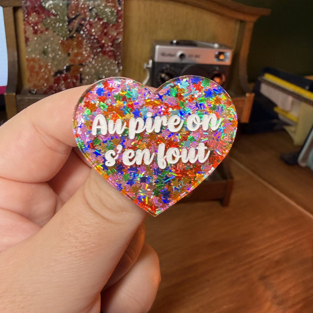 Broche "Au pire on s'en fout" en acrylique semi transparente avec des étoiles multicolores