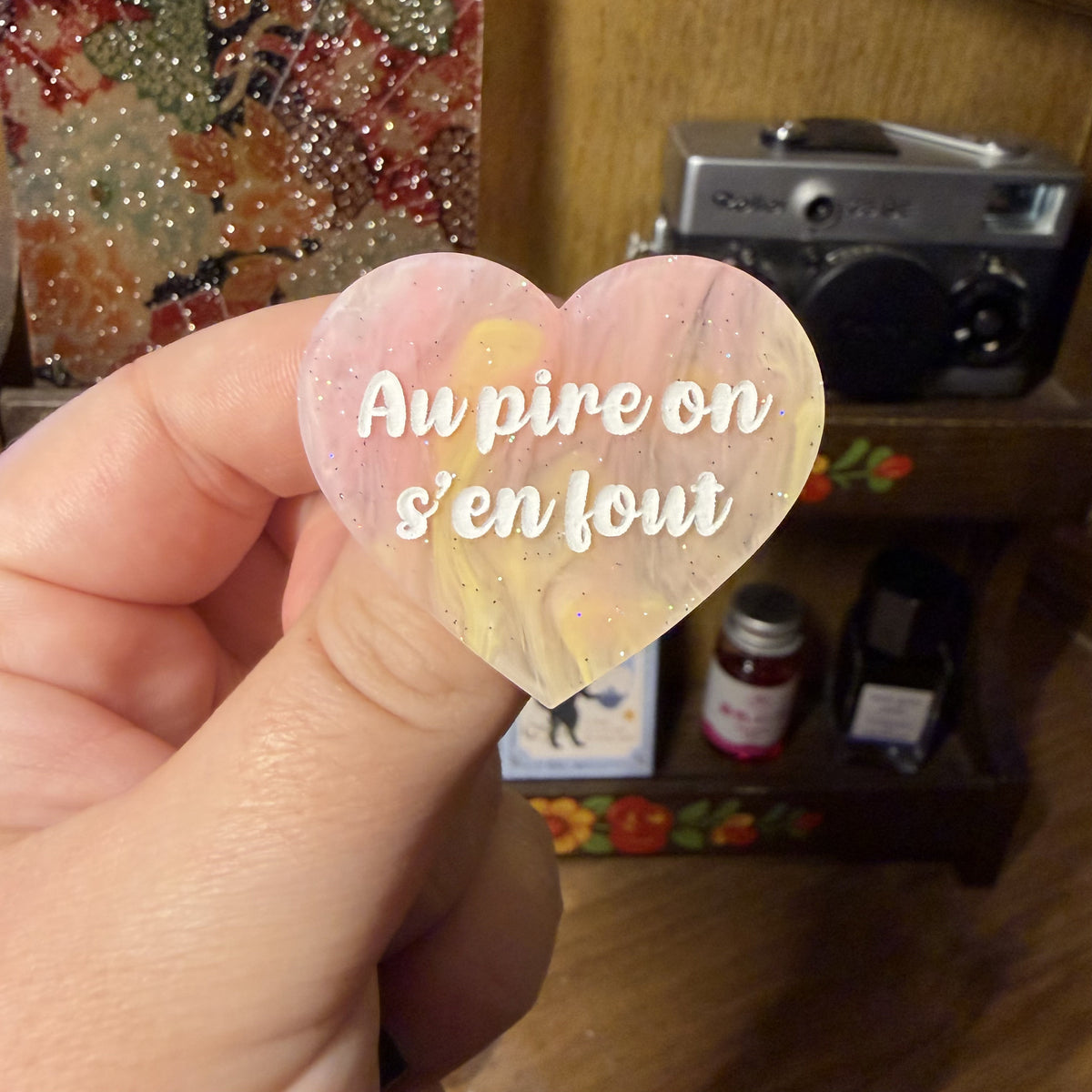Broche "Au pire on s'en fout" en acrylique semi transparente marbrée corail, orange et jaune à paillettes