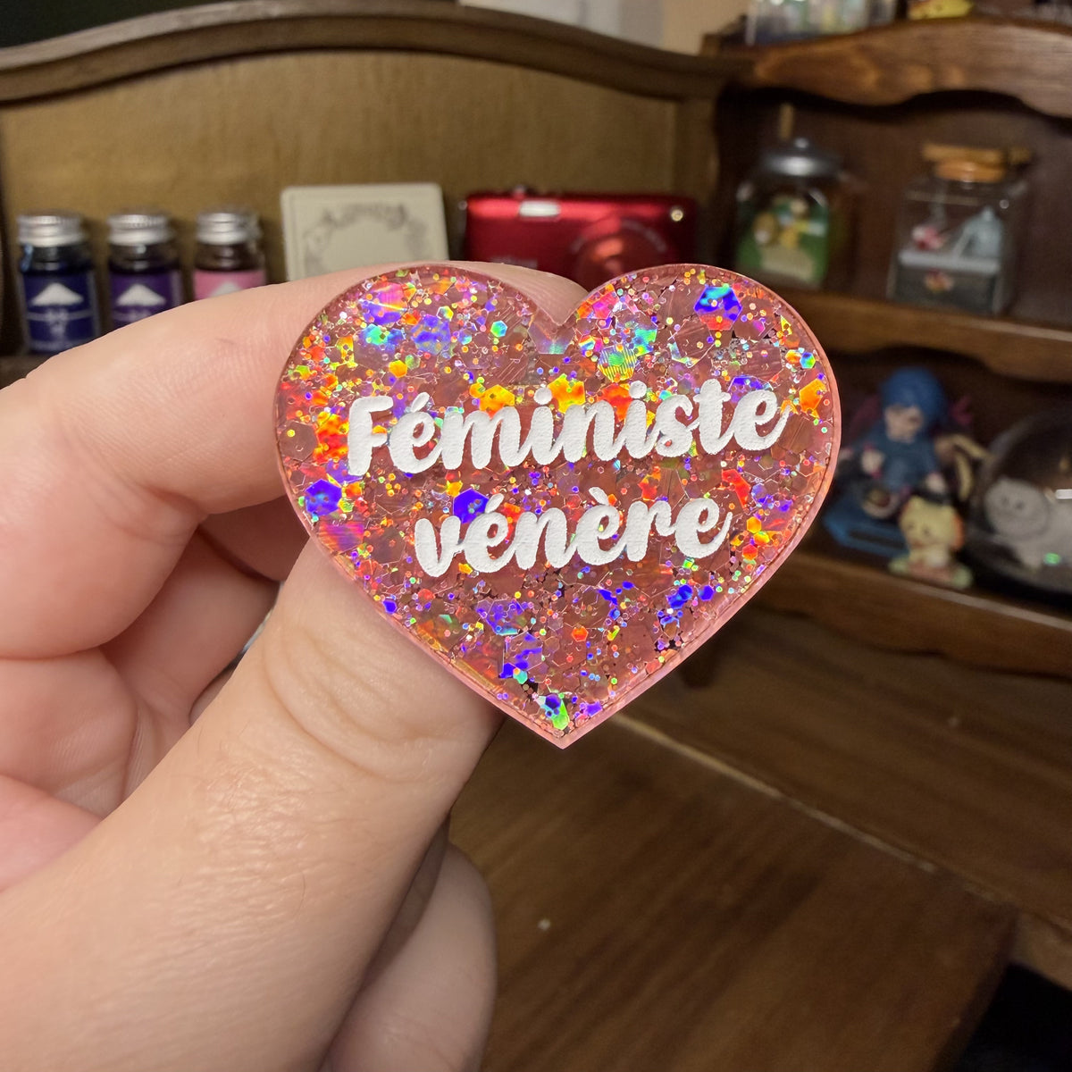 Broche "Féministe vénère" en acrylique semi transparente avec des paillettes corail