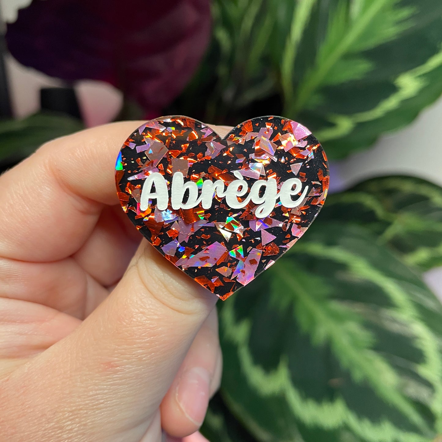 Broche "Abrège" en acrylique noire avec des éclats de confettis rouges et roses