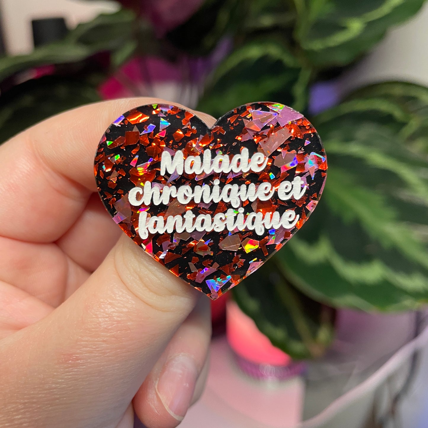 Broche "Malade chronique et fantastique" en acrylique noire avec des éclats de confettis rouges et roses