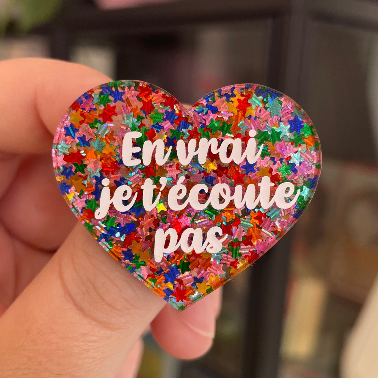 Broche "En vrai je t'écoute pas" en acrylique semi-transparente avec des confettis étoiles multicolores