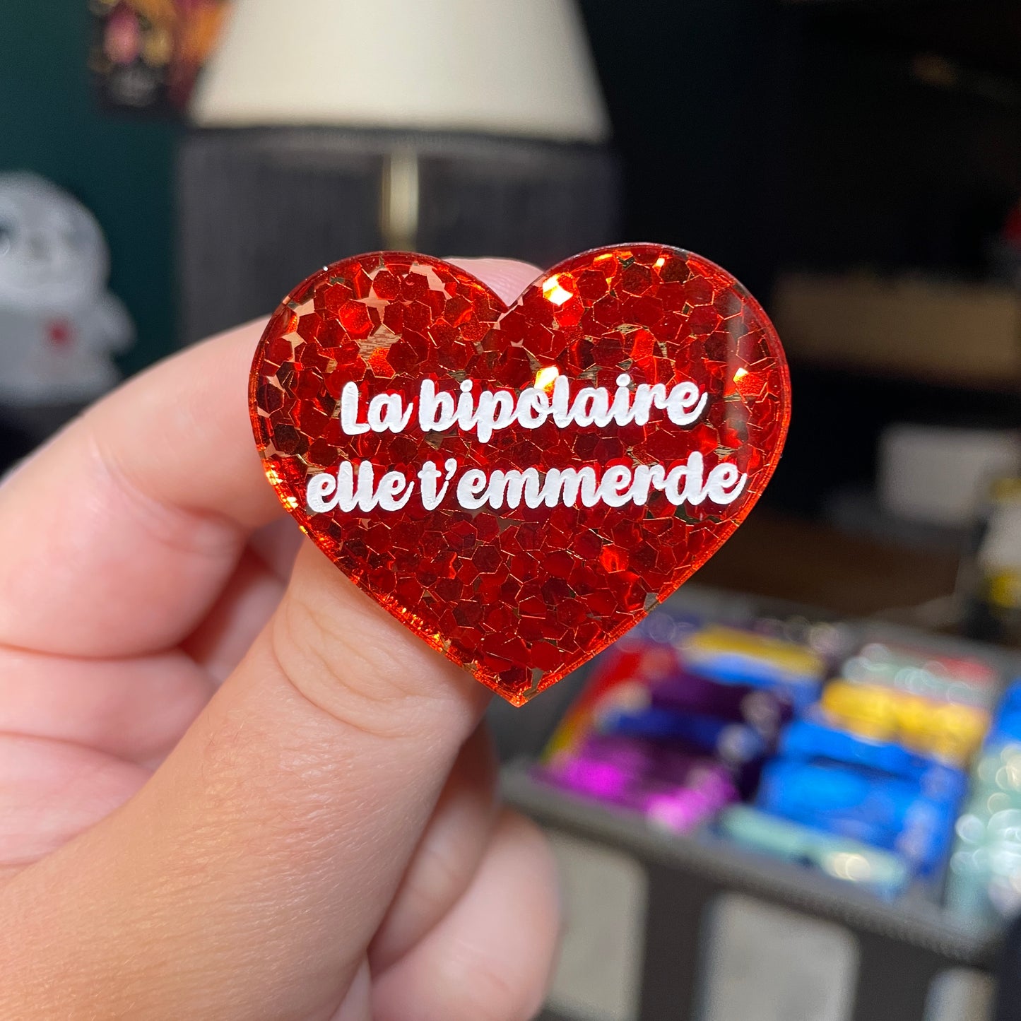 Broche "La bipolaire elle t'emmerde" en acrylique semi transparente avec des confettis rouges