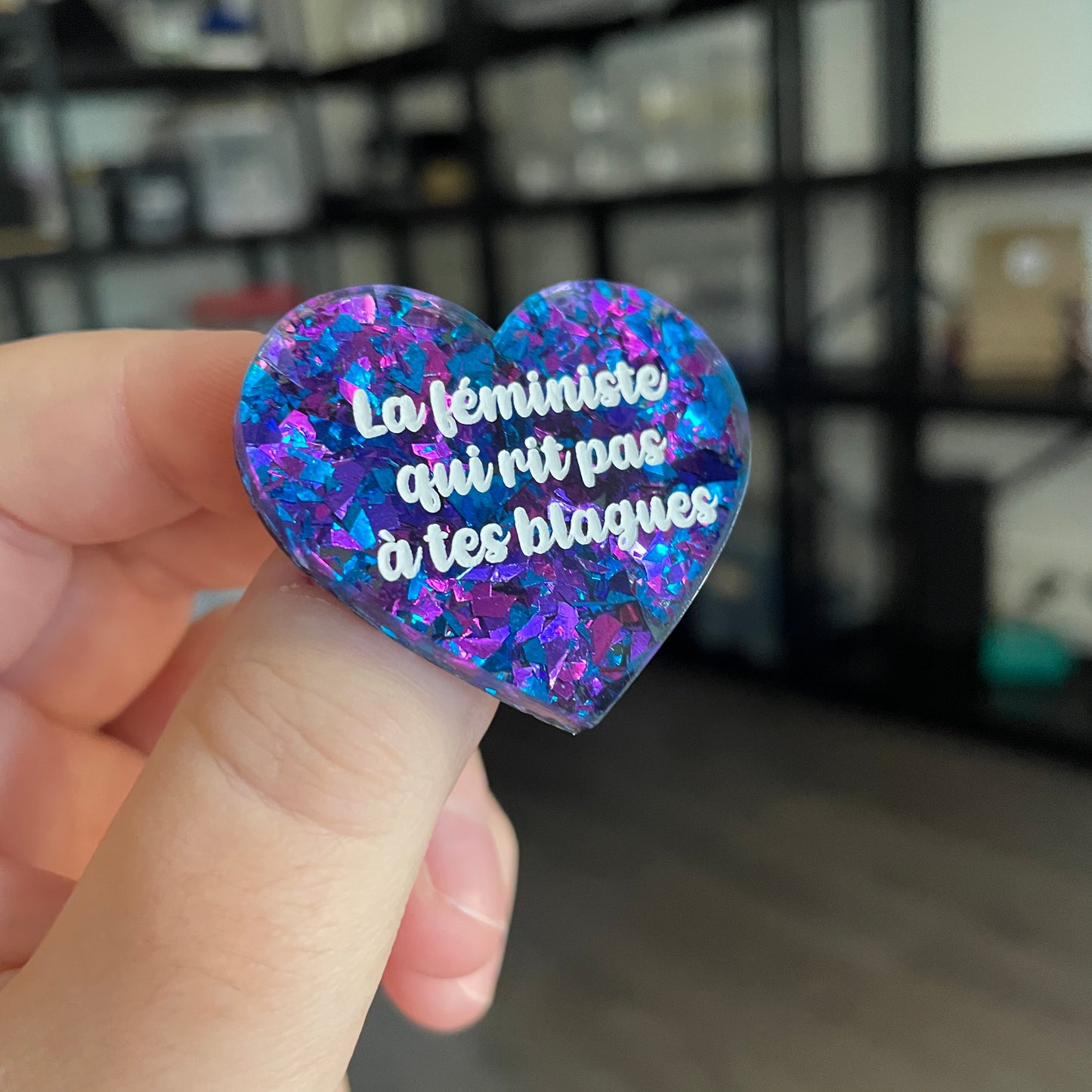 Broche "La féministe qui rit pas à tes blagues" en acrylique transparente avec des éclats de confettis bleus et violets