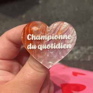 Broche "Champion’e du quotidien" en acrylique marbrée orange, blanche et mauve à paillettes
