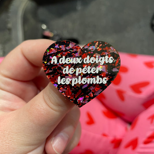 Broche "A deux doigts de péter lés plombs" en acrylique noire avec des éclats de confettis rouges et roses