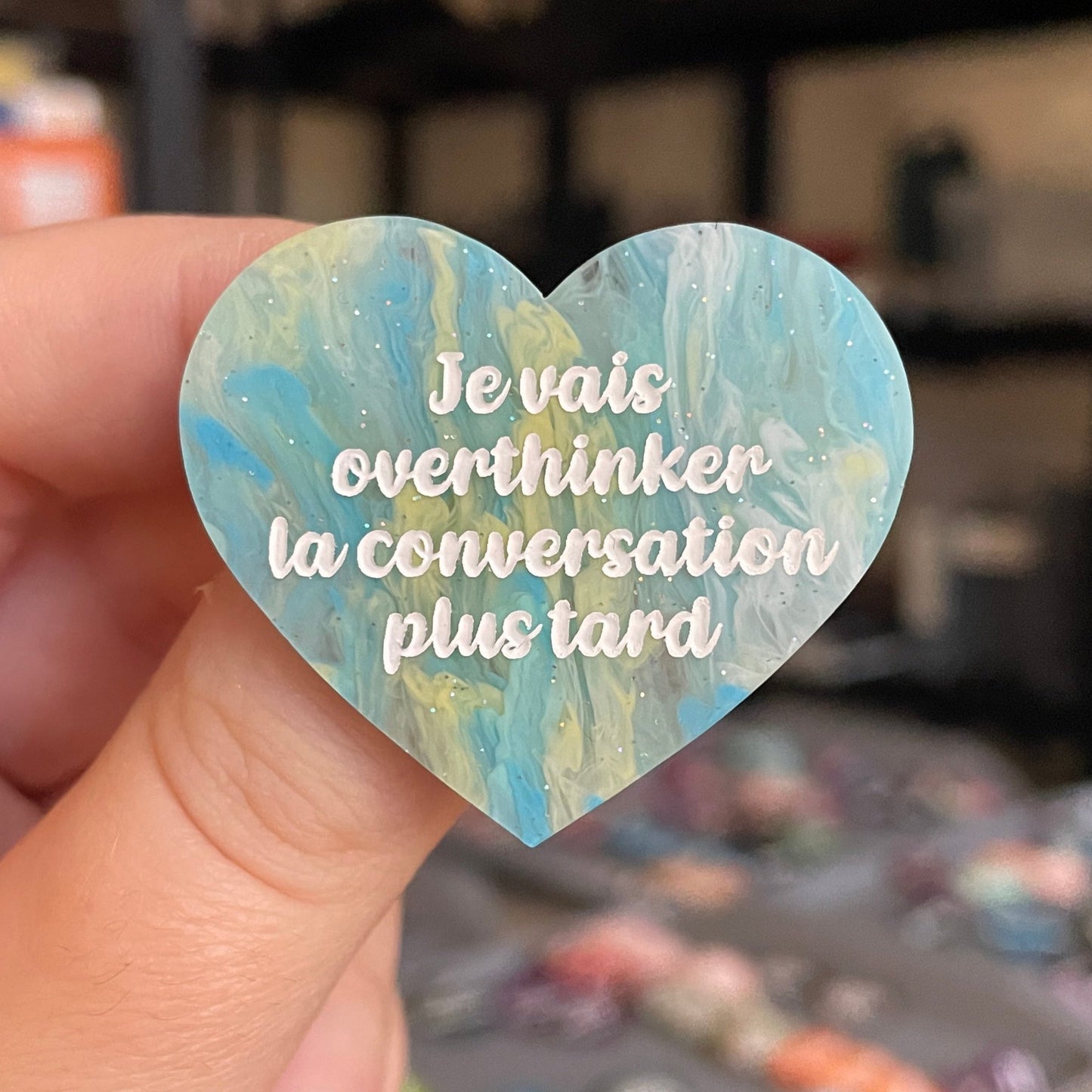 Broche "Je vais overthinker la conversation plus tard" en acrylique marbrée semi-transparente bleue, turquoise, blanche et jaune à paillettes