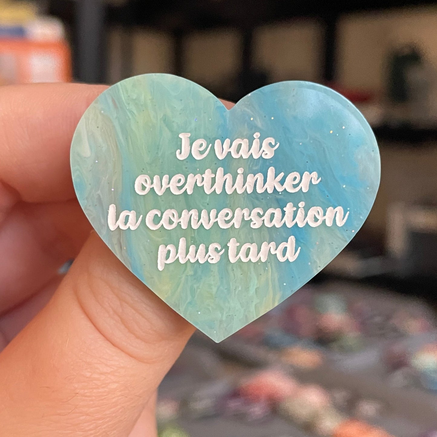 Broche "Je vais overthinker la conversation plus tard" en acrylique marbrée semi-transparente bleue, turquoise, blanche et jaune à paillettes