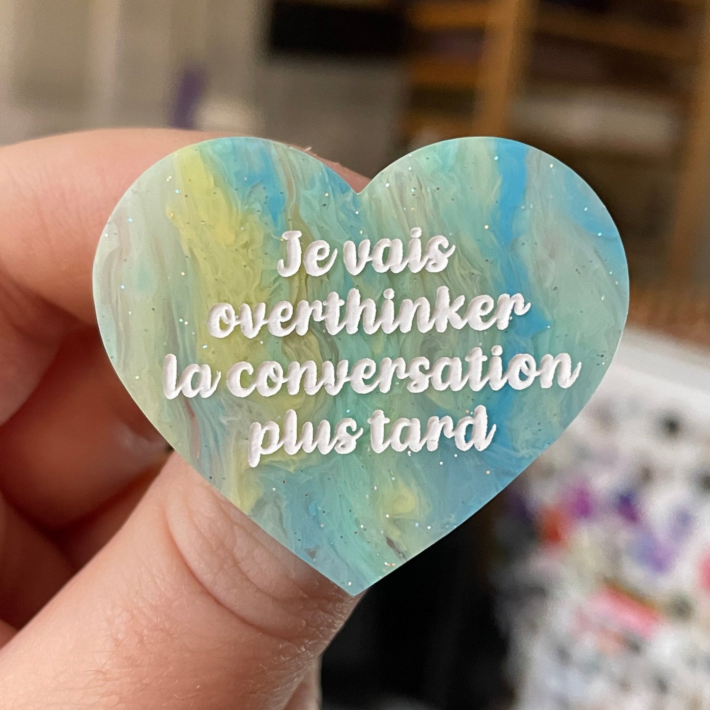 Broche "Je vais overthinker la conversation plus tard" en acrylique marbrée semi-transparente bleue, turquoise, blanche et jaune à paillettes