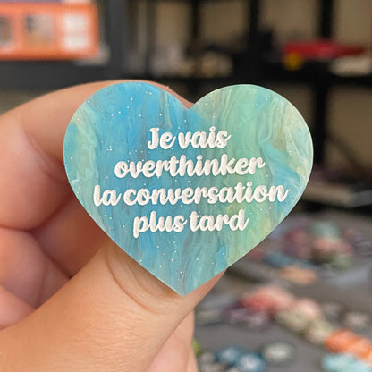 Broche "Je vais overthinker la conversation plus tard" en acrylique marbrée semi-transparente bleue, turquoise, blanche et jaune à paillettes