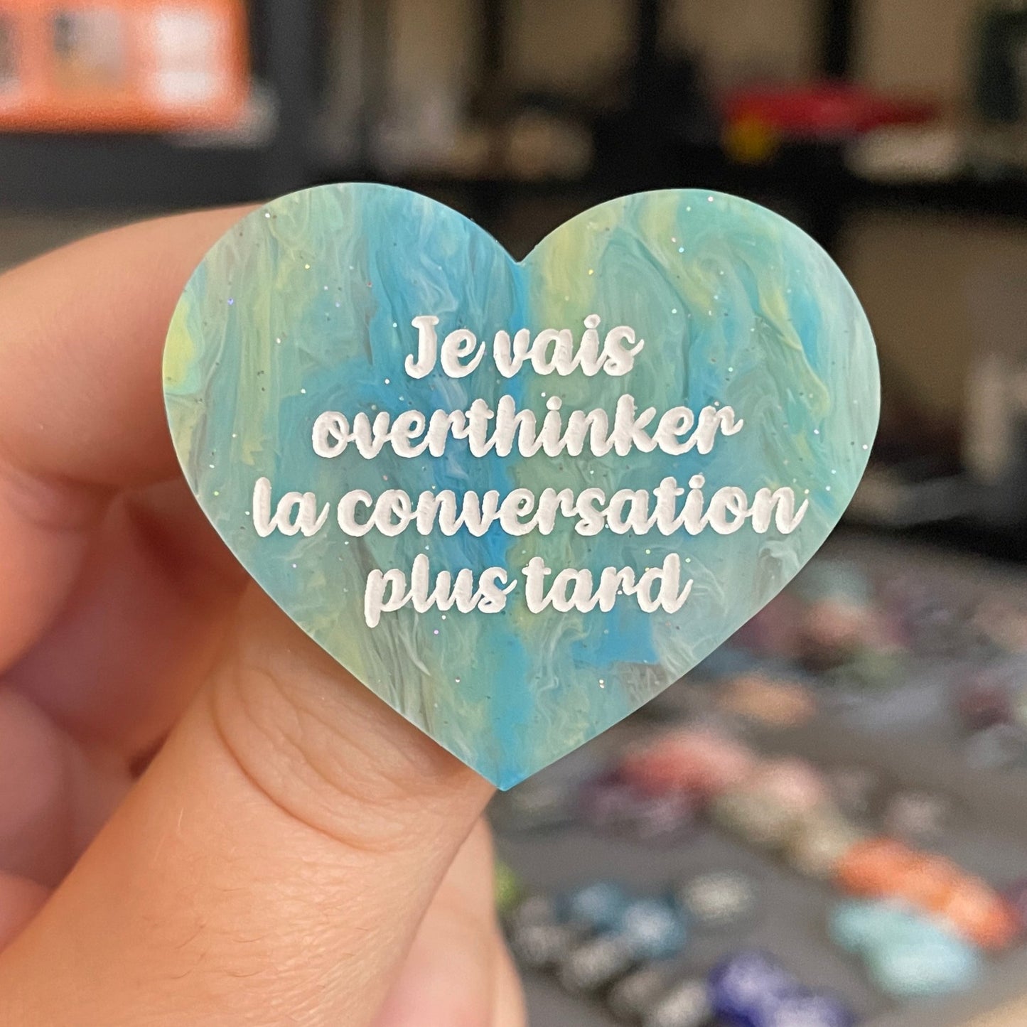 Broche "Je vais overthinker la conversation plus tard" en acrylique marbrée semi-transparente bleue, turquoise, blanche et jaune à paillettes