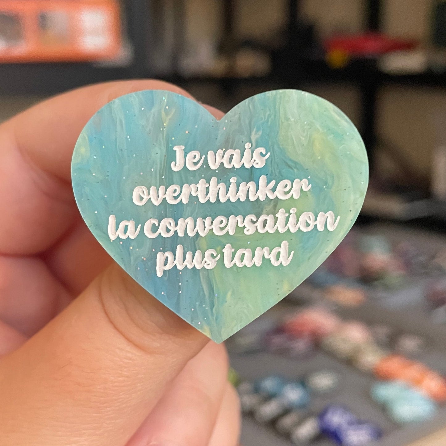Broche "Je vais overthinker la conversation plus tard" en acrylique marbrée semi-transparente bleue, turquoise, blanche et jaune à paillettes