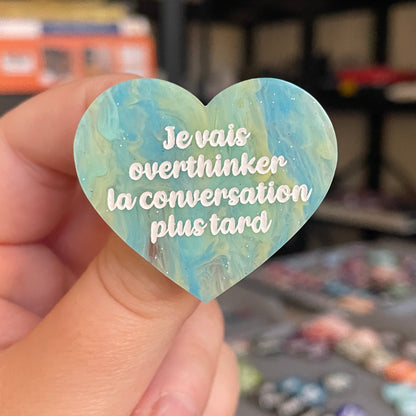 Broche "Je vais overthinker la conversation plus tard" en acrylique marbrée semi-transparente bleue, turquoise, blanche et jaune à paillettes