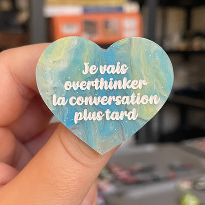 Broche "Je vais overthinker la conversation plus tard" en acrylique marbrée semi-transparente bleue, turquoise, blanche et jaune à paillettes