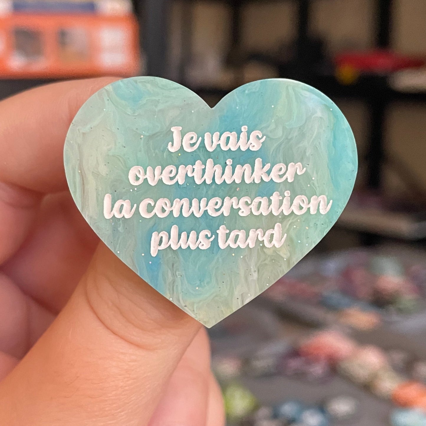 Broche "Je vais overthinker la conversation plus tard" en acrylique marbrée semi-transparente bleue, turquoise, blanche et jaune à paillettes
