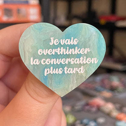 Broche "Je vais overthinker la conversation plus tard" en acrylique marbrée semi-transparente bleue, turquoise, blanche et jaune à paillettes