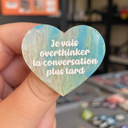 Broche "Je vais overthinker la conversation plus tard" en acrylique marbrée semi-transparente bleue, turquoise, blanche et jaune à paillettes