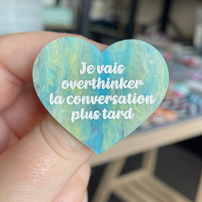 [CONTRÔLE TECHNIQUE] Broche "Je vais overthinker la conversation plus tard" en acrylique marbrée semi-transparente bleue, turquoise, blanche et jaune à paillettes