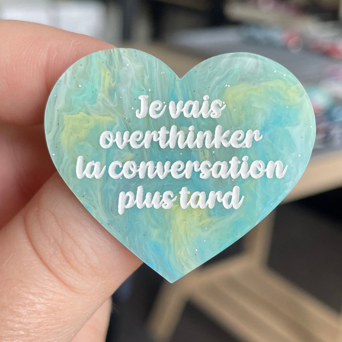 [CONTRÔLE TECHNIQUE] Broche "Je vais overthinker la conversation plus tard" en acrylique marbrée semi-transparente bleue, turquoise, blanche et jaune à paillettes