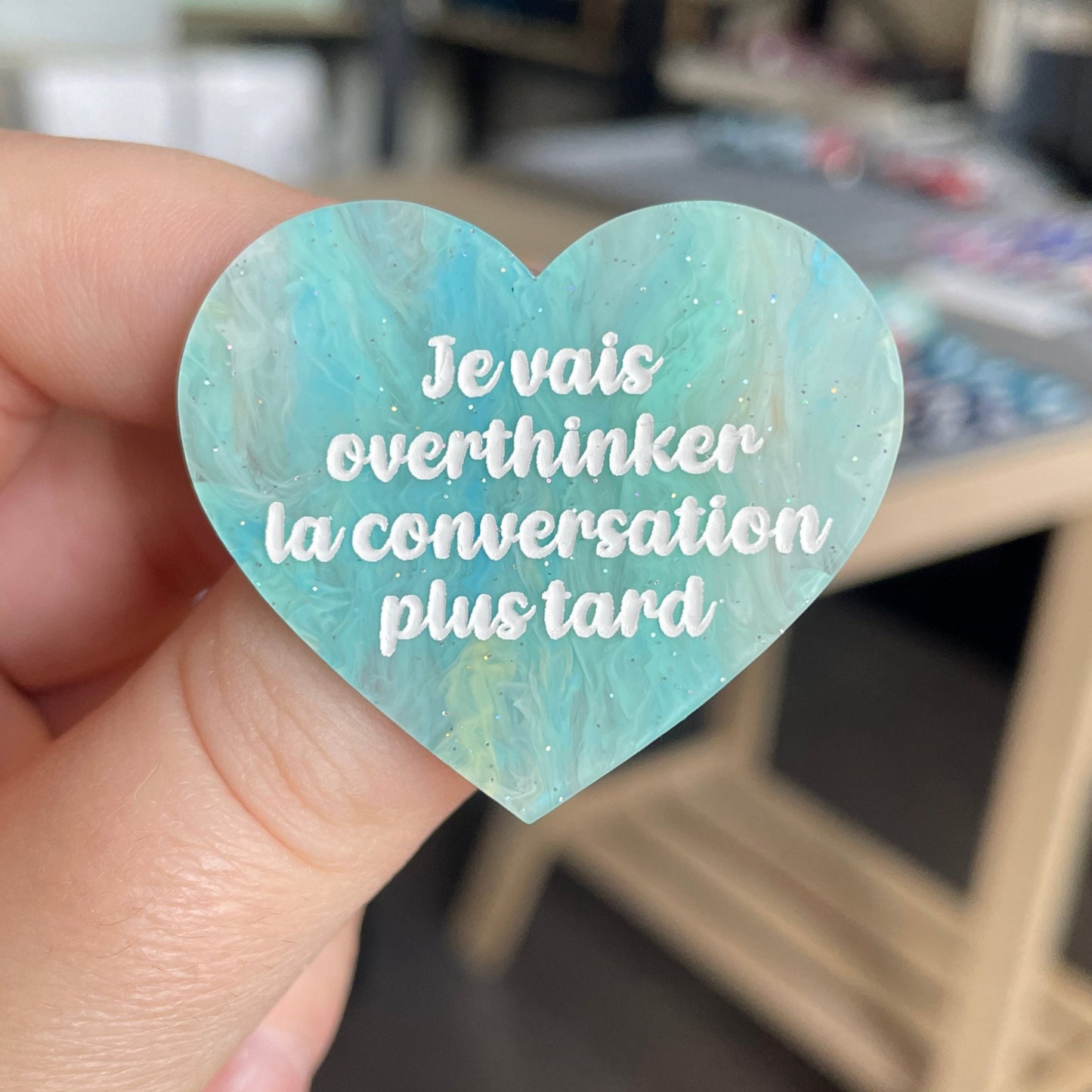 [CONTRÔLE TECHNIQUE] Broche "Je vais overthinker la conversation plus tard" en acrylique marbrée semi-transparente bleue, turquoise, blanche et jaune à paillettes