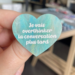[CONTRÔLE TECHNIQUE] Broche "Je vais overthinker la conversation plus tard" en acrylique marbrée semi-transparente bleue, turquoise, blanche et jaune à paillettes