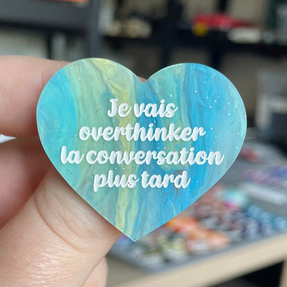[CONTRÔLE TECHNIQUE] Broche "Je vais overthinker la conversation plus tard" en acrylique marbrée semi-transparente bleue, turquoise, blanche et jaune à paillettes