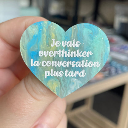 [CONTRÔLE TECHNIQUE] Broche "Je vais overthinker la conversation plus tard" en acrylique marbrée semi-transparente bleue, turquoise, blanche et jaune à paillettes