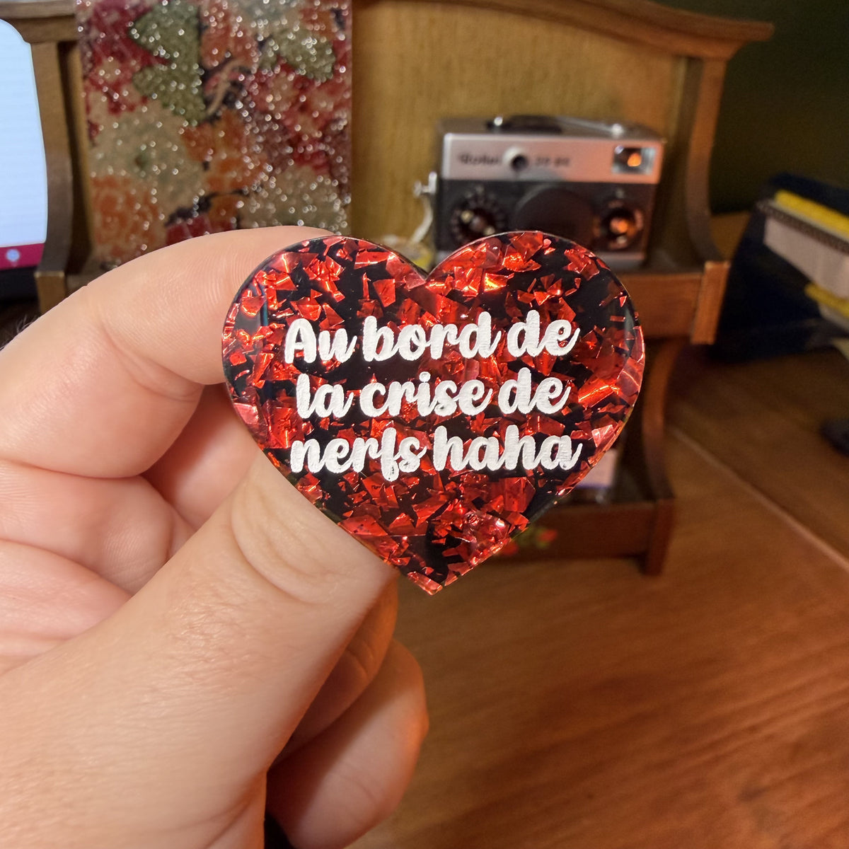 Broche "Au bord de la crise de nerfs haha" en acrylique noire avec des éclats de confettis rouges