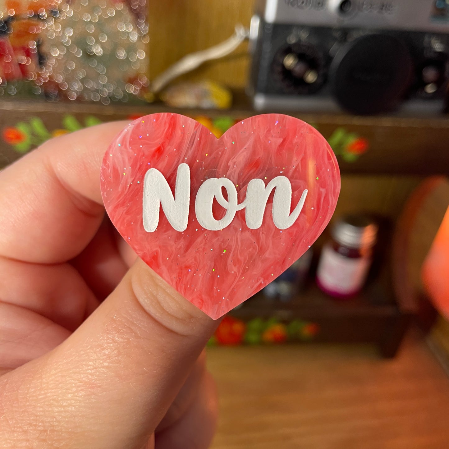 Broche "Non" en acrylique semi transparente marbrée rouge et rose à paillettes