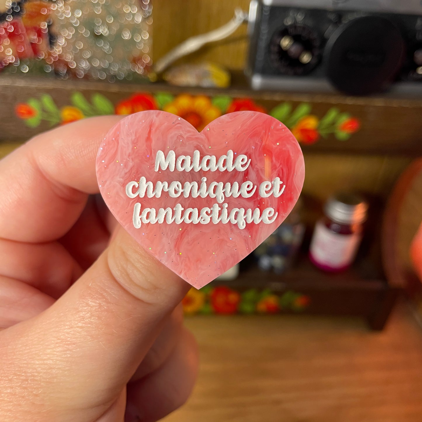 Broche "Malade chronique et fantastique" en acrylique semi transparente marbrée rouge et rose à paillettes