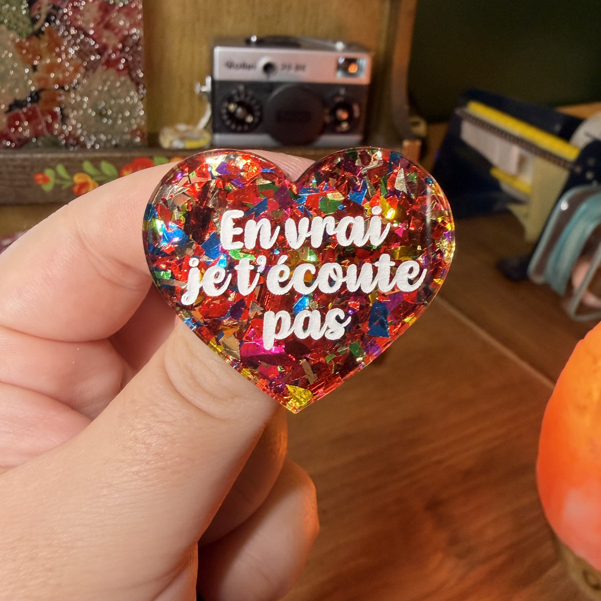 Broche "En vrai je t'écoute pas" en acrylique transparente avec des confettis rouges et multicolores