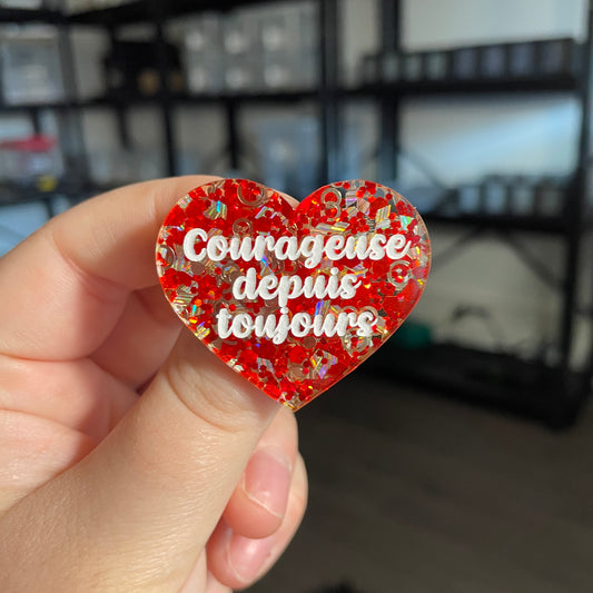 Broche "Courageuse depuis toujours" en acrylique semi transparente avec des confettis rouges et argentés