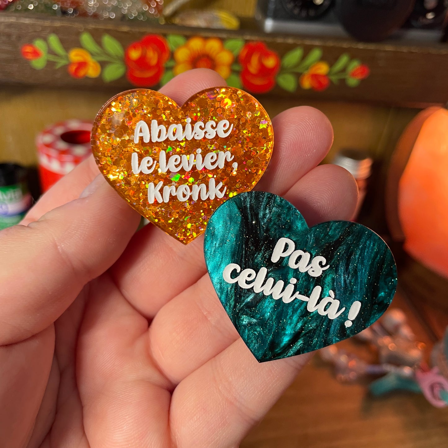 Duo de broches "Abaisse le levier, Kronk !" et "Pas celui-là !" en acrylique semi transparente à paillettes oranges et en acrylique marbrée verte et noire à paillettes