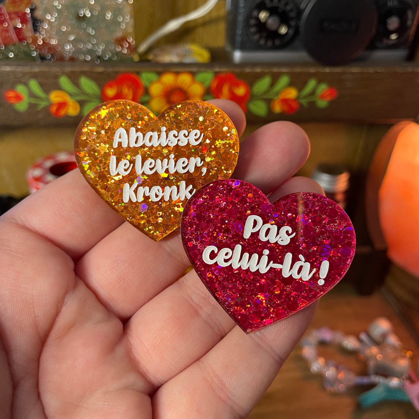 Duo de broches "Abaisse le levier, Kronk !" et "Pas celui-là !" en acrylique semi transparente à paillettes oranges et en acrylique semi transparente à paillettes rouges