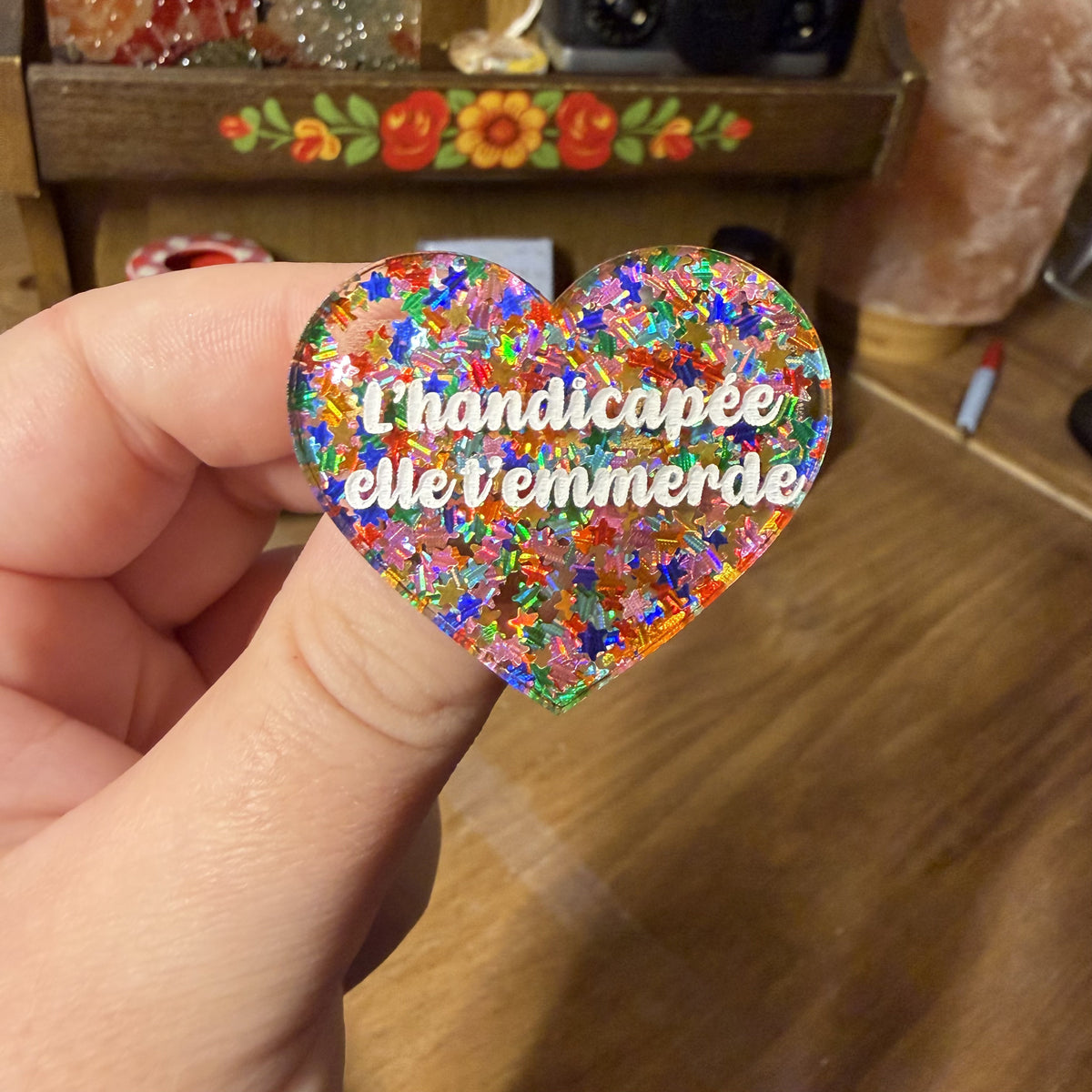 [Contrôle technique] Broche "L'handicapée elle t'emmerde" en acrylique semi transparente avec des étoiles multicolores