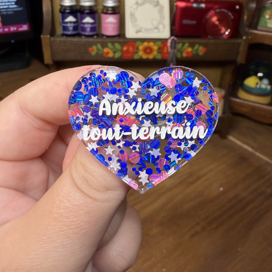 Broche "Anxieuse tout-terrain" en acrylique semi transparente avec des confettis bleus, roses et blancs