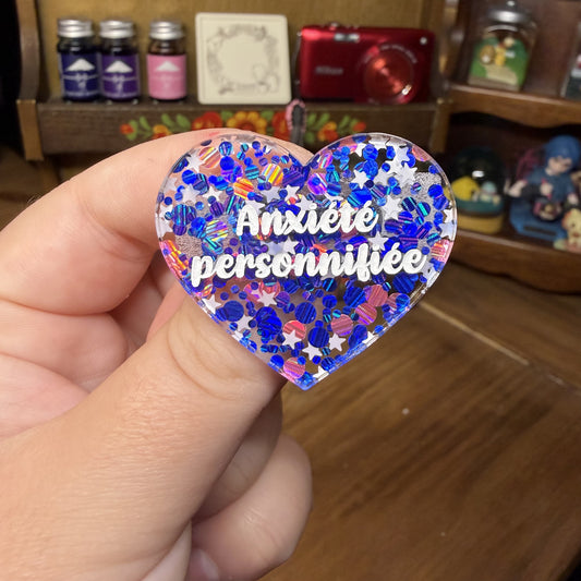 Broche "Anxiété personnifée" en acrylique semi transparente avec des confettis bleus, roses et blancs