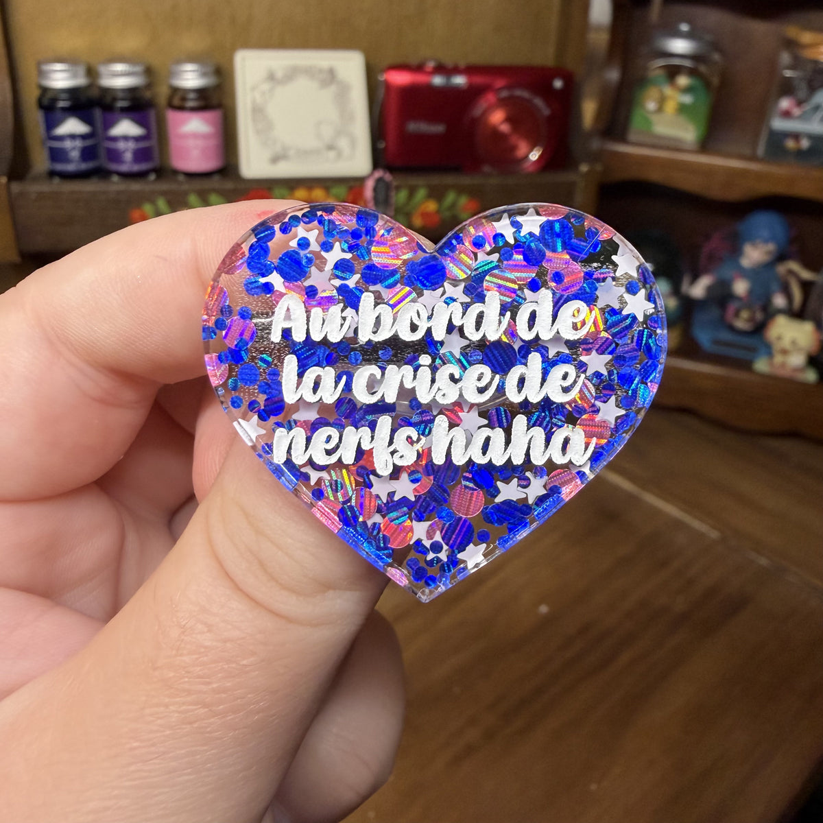Broche "Au bord de la crise de nerfs haha" en acrylique semi transparente avec des confettis bleus, roses et blancs