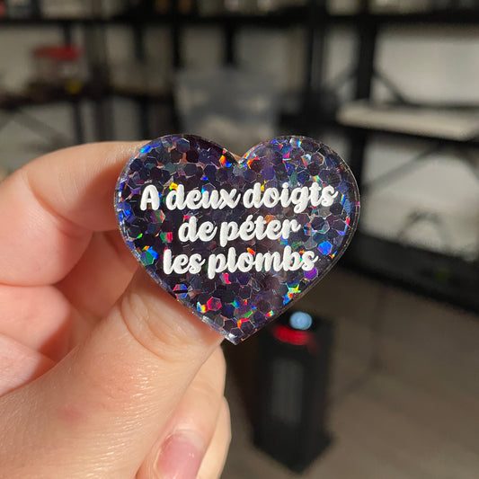 Broche "A deux doigts de péter les plombs" en acrylique semi transparente avec des confettis noirs