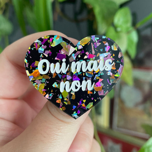 Broche "Oui mais non" en acrylique noire avec des éclats de confettis multicolores