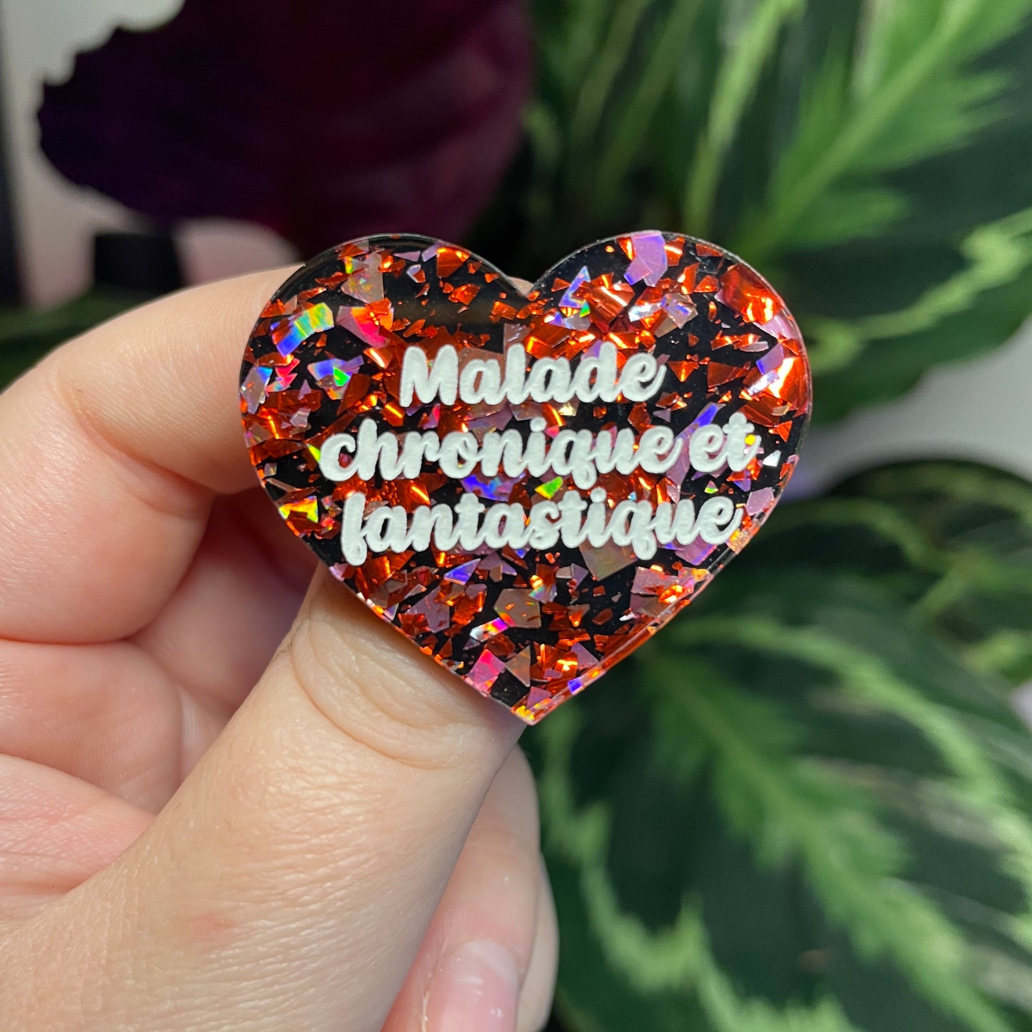 Broche "Malade chronique et fantastique" en acrylique noire avec des éclats de confettis rouges et roses