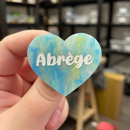 Broche "Abrège" en acrylique marbrée semi-transparente bleue, turquoise, blanche et jaune à paillettes