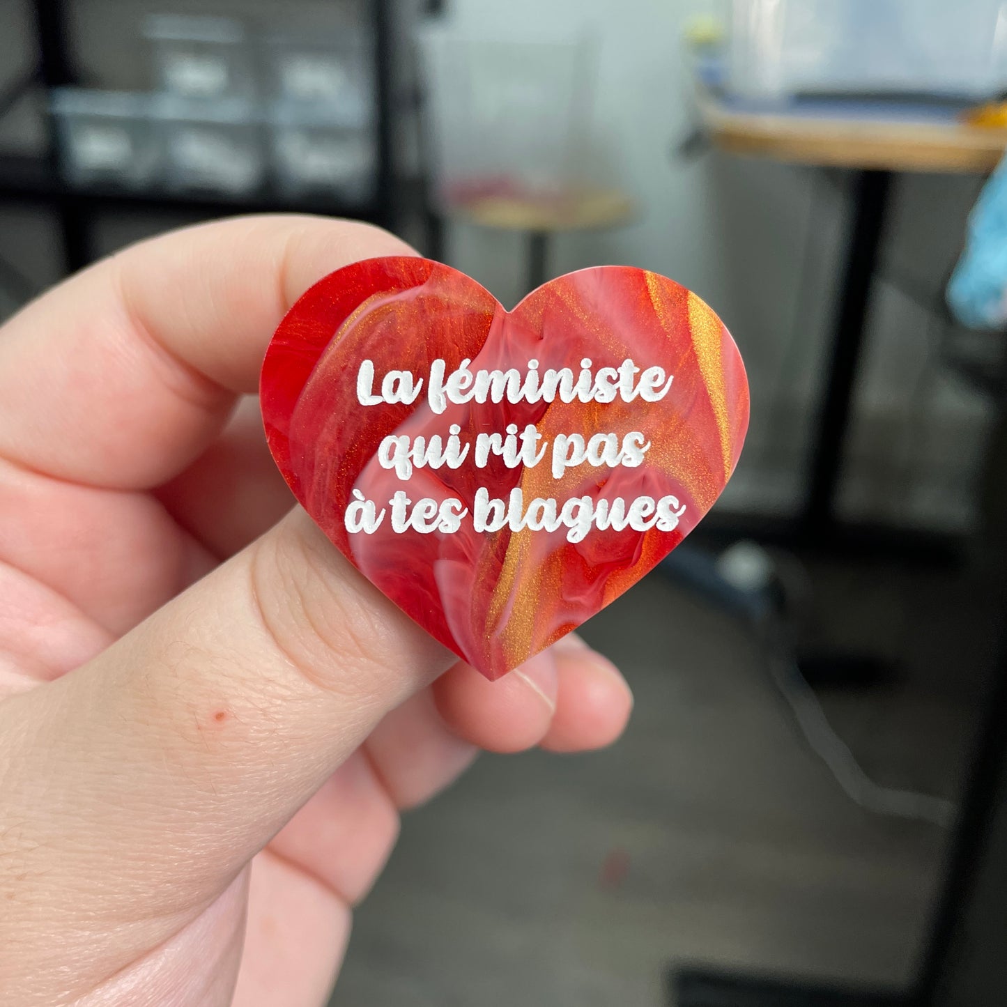 Broche "La féministe qui rit pas à tes blagues" en acrylique marbrée rouge, blanche et dorée