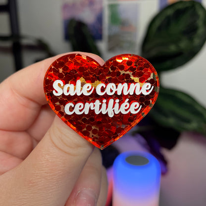 Broche "Sale conne certifiée" en acrylique semi transparente avec des confettis rouges