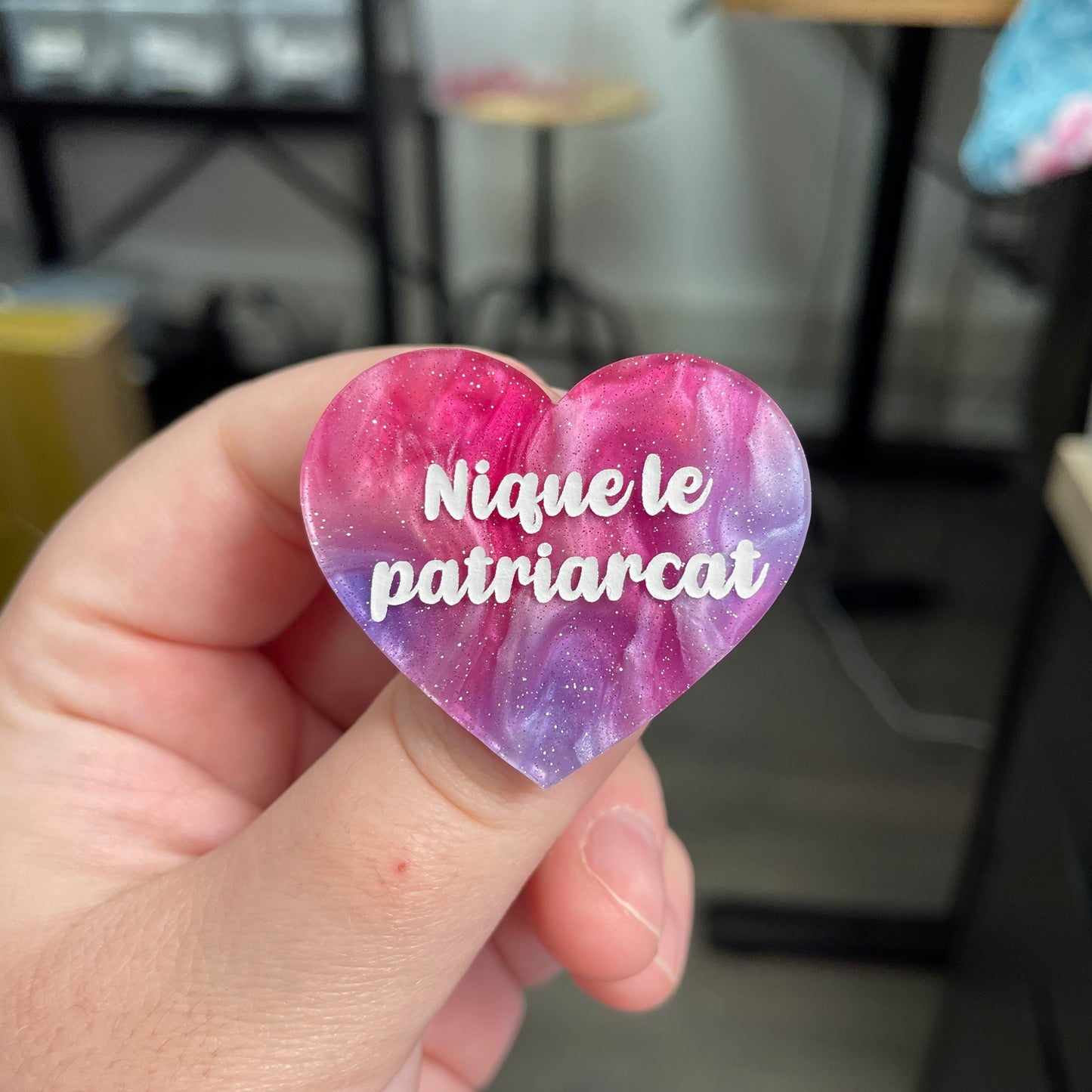 Broche "Nique le patriarcat" en acrylique marbrée bleue, rose et blanche à paillettes