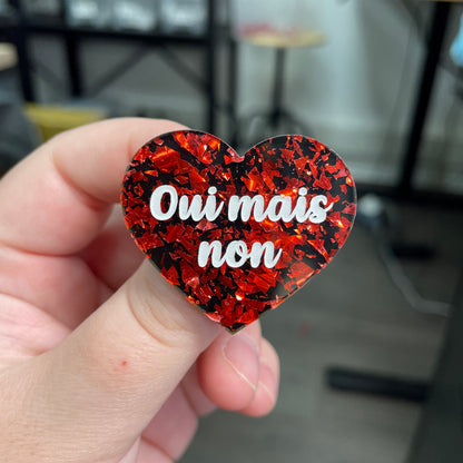 Broche "Oui mais non" en acrylique noire avec des éclats de confettis rouges
