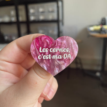 [CONTRÔLE TECHNIQUE] Broche "Les cernes, c'est pas DA" en acrylique marbrée rose et blanche à paillettes