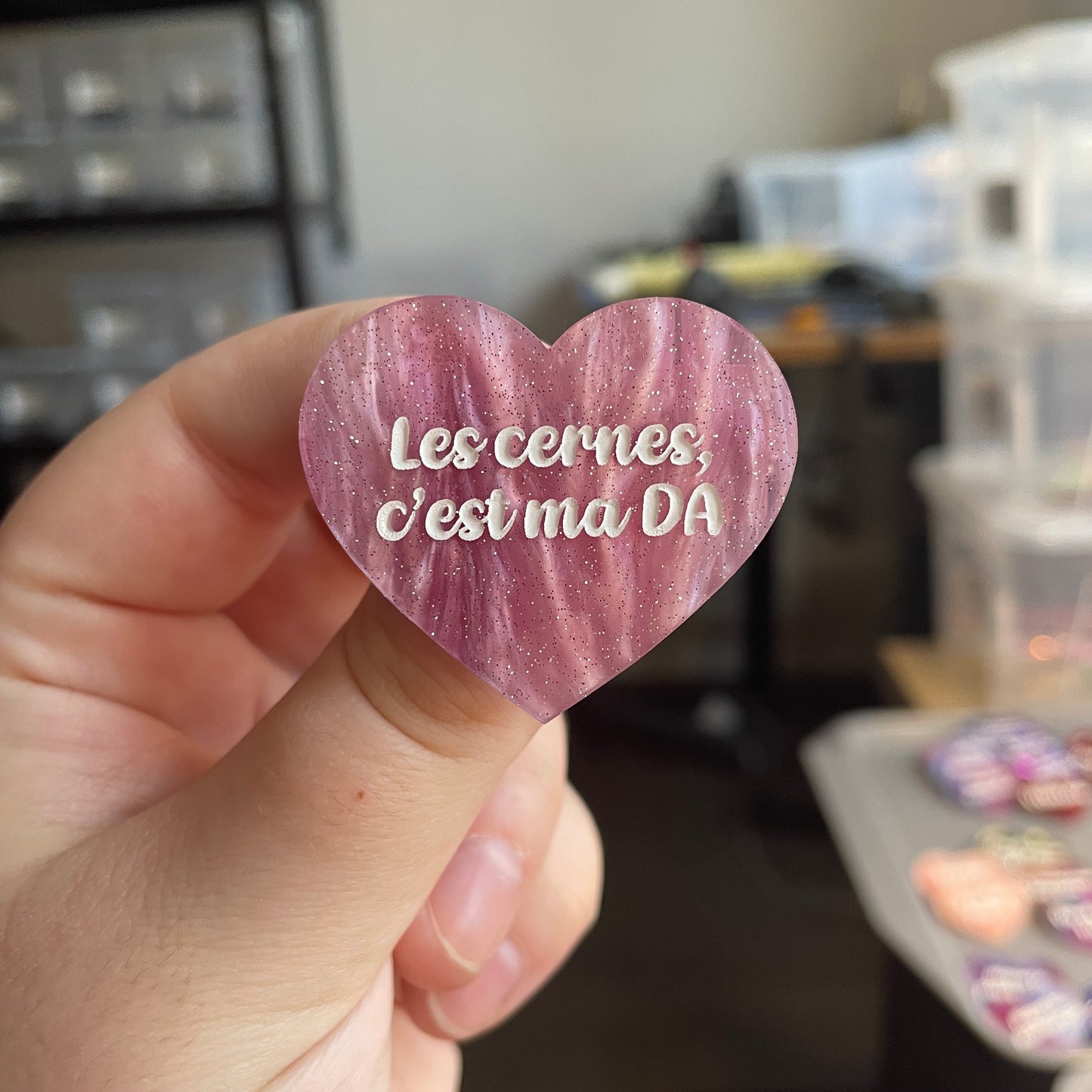 [CONTRÔLE TECHNIQUE] Broche "Les cernes, c'est pas DA" en acrylique marbrée rose et blanche à paillettes